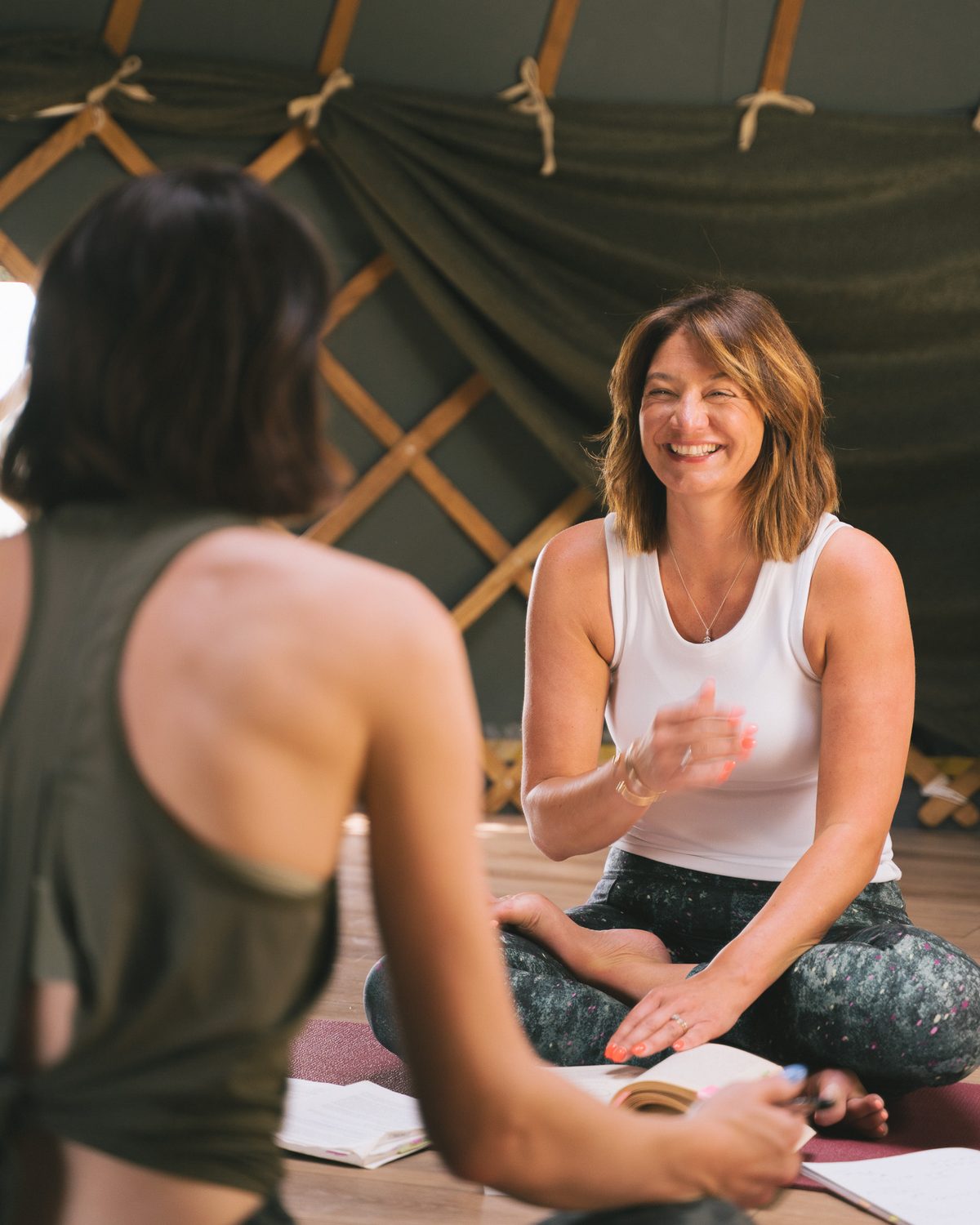 Lucy King laughing while teaching a seated student inside a canvas yurt
