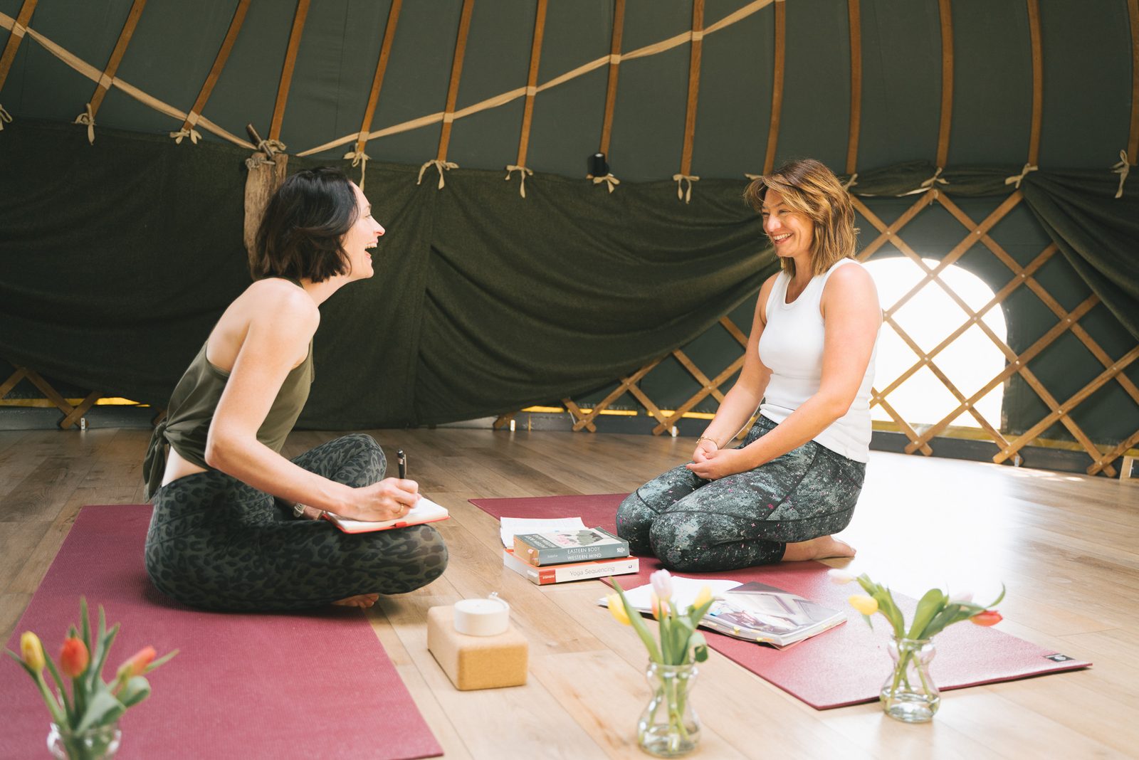 Lucy and a student sitting cross-legged on mats, talking, inside a yurt